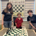 two teens alongside a young boy, in front of a giant chess board