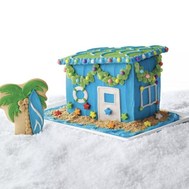 gingerbread house decorated to look like a beach cabana, with blue icing walls and palm tree cookie