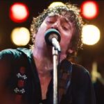 man soaked with sweat on stage singing into microphone