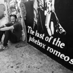 black and white photo of man sitting besides outdoor mural