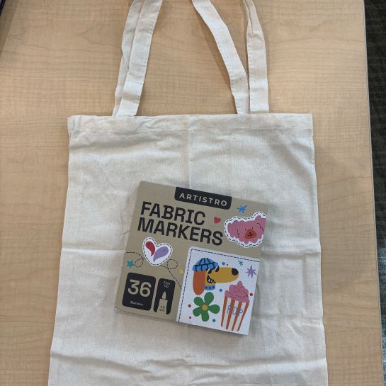 plain white tote bag laying flat on table with package of fabric markers on top