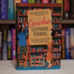 Book with cover illustration of man climbing a library shelf ladder and woman pushing bookcart, below book title "Overdue"