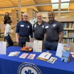 Three men in ems uniforms standing behind a table