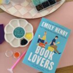 a partitioned tray containing colored beads, alongside a paperback book titled Book Lovers