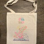 Tote bag with stencil graphic of a book opened flat and flowers rising from it