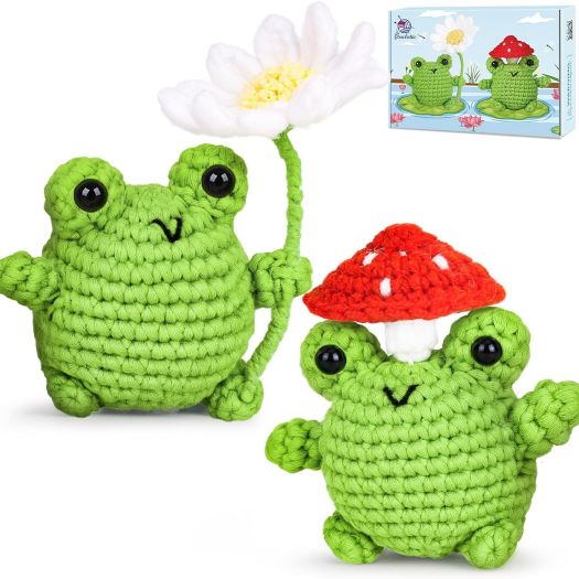 two crochet green frogs, one holding white daisy, the other with toadstool on head