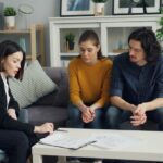worried looking young couple sitting down with a female financial planner