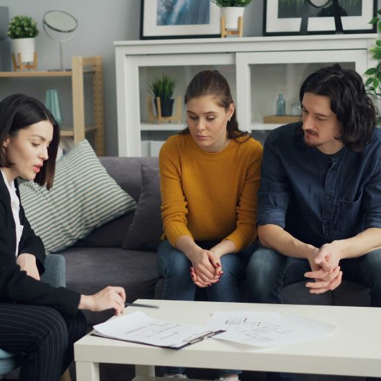 worried looking young couple sitting down with a female financial planner