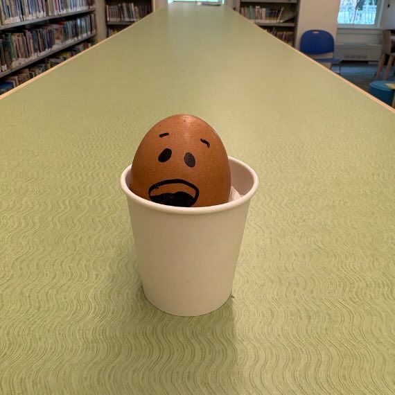 An egg with a scared expression drawn on its shell with marker is inside a paper cup