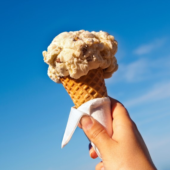 Hand holding a cone of ice cream against the sky