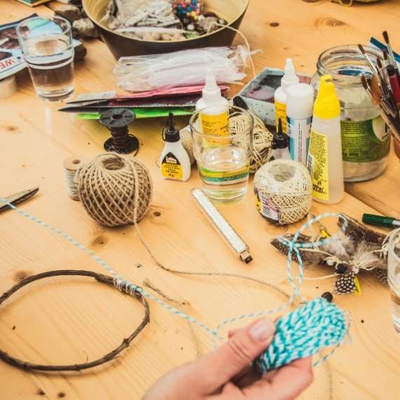 Assorted craft items on a table as a hand holds twine.