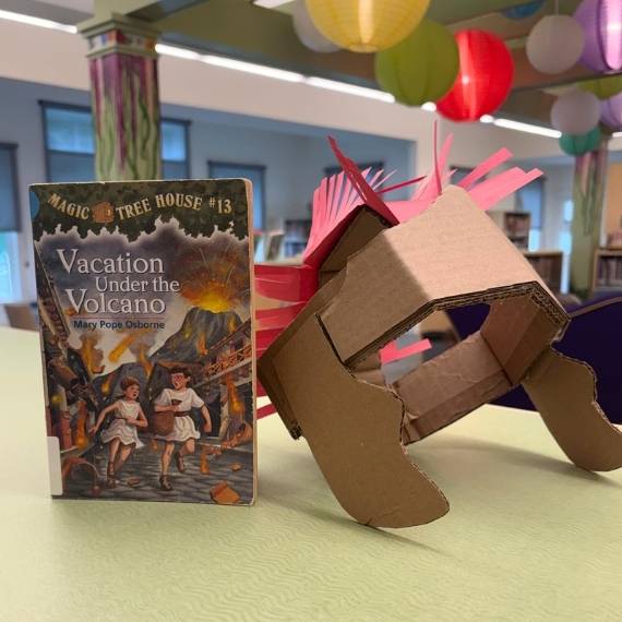 Book 13 in Magic Tree House Series next to a gladiator helmet made out of cardboard.