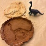 A dinosaur toy, a piece of clay with the imprint of a dinosaur, and a dried clay fossil of a dinosaur.
