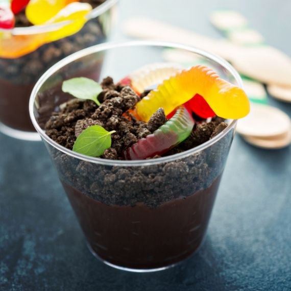 A cup of chocolate pudding with cookie crumble and gummy worms.