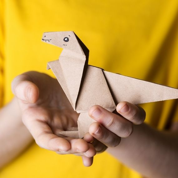 Hands holding a paper origami craft in the shape of a dinosaur.