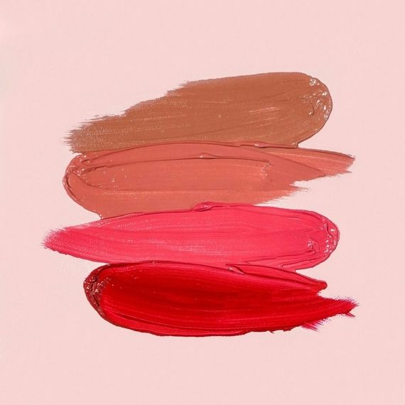 Four shades of red and brown lip gloss smeared on a pink background.