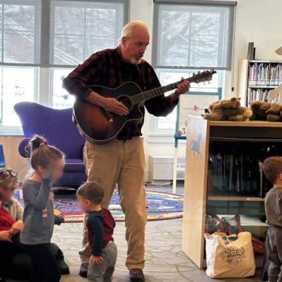 Older man playing guitar surrounded by dancing children
