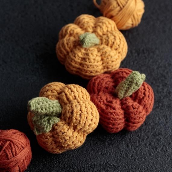 Three pumpkins created out of yarn and two balls of yarn on a black background