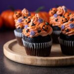 Four chocolate cupcakes decorated with orange frosting and Halloween-themed toppings.