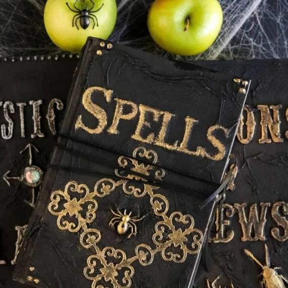 Spell books on top of table with two green apples and a spider