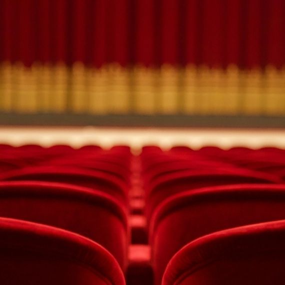 Red seats in a theatre with closed curtain and stage in background.