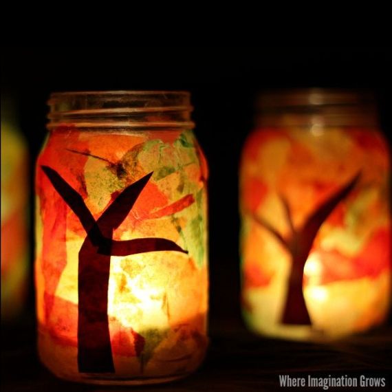 Two mason jars decorated with papers in shape of trees with lights inside them
